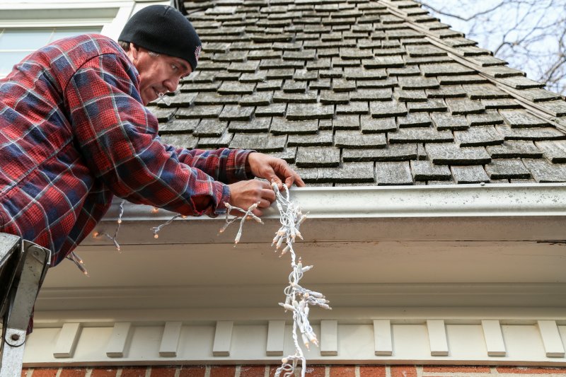 A man hanging Christmas lights on his gutters.