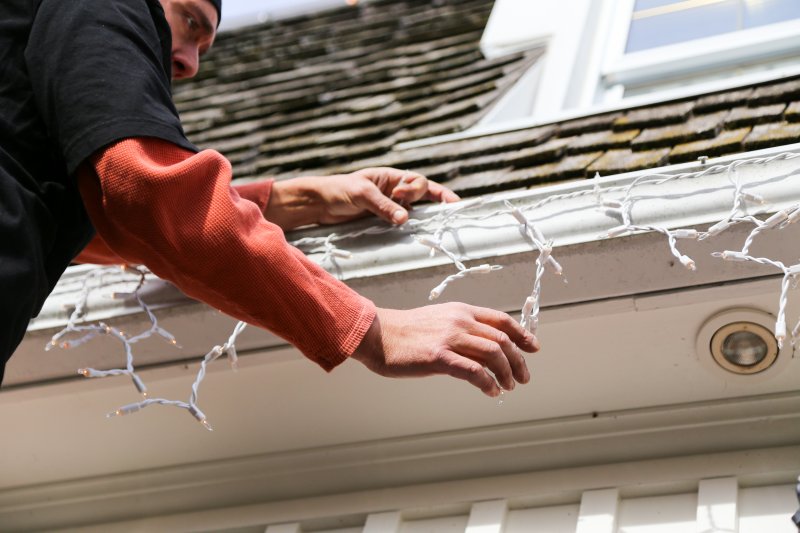 man hanging Christmas lights on gutters